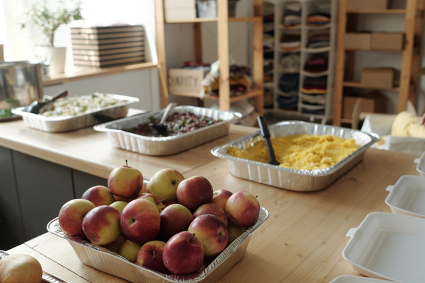 Apples and buns are in aluminum form on the table  with empty disposable containers and aluminum forms with food