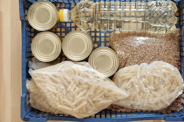 Canned food is packed into a dark blue plastic crate with bottled oil packages of pasta and buckwheat