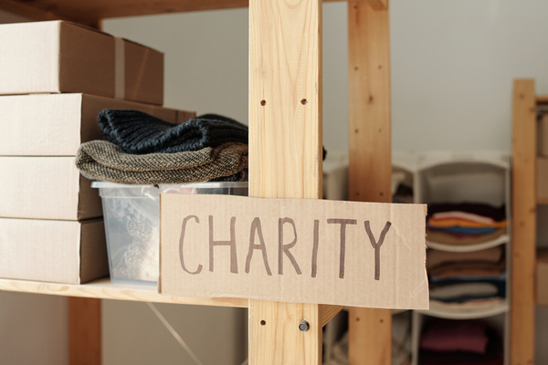 Inscription charity is on a cardboard sign on a wooden rack with boxes and a plastic container filled with items of clothing