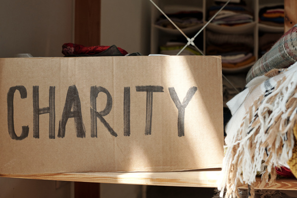 Inscription about charity is on the cardboard sign which is on a wooden shelf near with pieces of clothing
