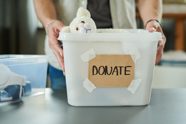 A man holds a container with two hands with an inscription about donations and with a white stuffed animal inside