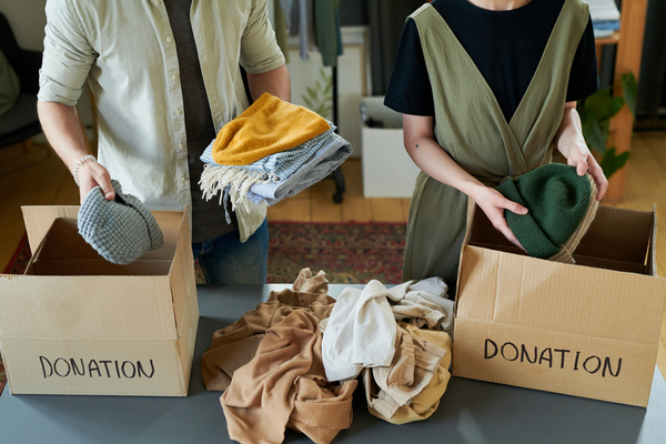 People put knitted hats of different colors and loght colored pieces of clothing in boxes with inscriptions about donation and a bundle of garments between them