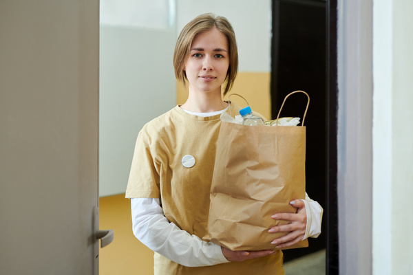 Female voluntary worker with short hair dressed in yellow t-shirt over white longsleeve with both hands holds craft charity package full of products