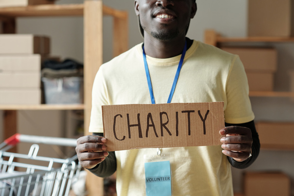 Smiling voluntary worker dresed in pale yellow uniform wearing blue badge holds cardboard sign with inscription about charity