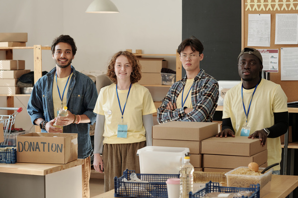 Young volunteers dressed in pale yellow T-shirts and with blue badges stand with donations packed in boxes and plastic crates filled with food for charity