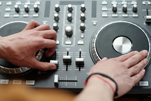 A man with bracelets on his arm makes music by spinning a disc and adjusting the sliders on the DJ console in black with silver elements