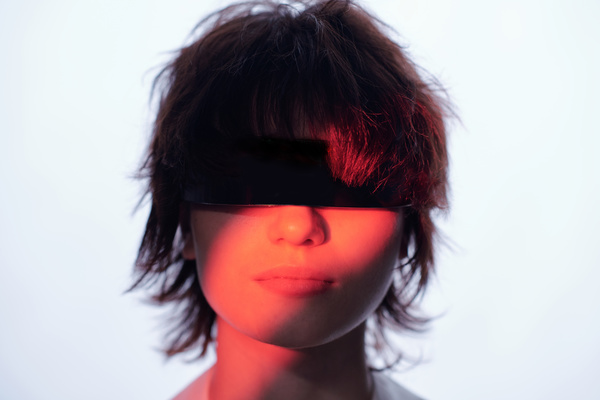 A close-up portrait of a young woman with short disheveled brown hair in the shade with a red neon light on her face