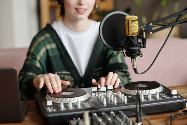 A smiling girl in a green cardigan makes music using a DJ console that stands on the table next to a microphone with a pop filter
