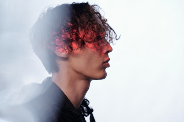 On a white background the profile of a young handsome curly-haired male cyberpunk wearing transparent plastic and glasses dressed in black