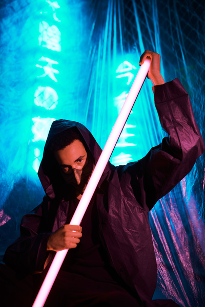 Cyberpunk ninja in a mask and dressed in black with a red lightsaber in his hands with blue neon glowing hieroglyphs and cellophane film on the background