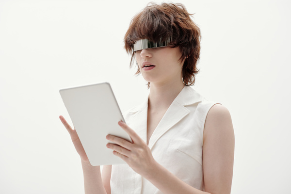 A girl with brown ruffled hair slightly open her mouth wearing cyberpunk style metal glasses wearing a white sleeveless blouse with a v-neck and collar holds a white tablet