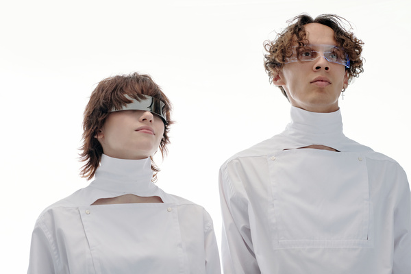 Futuristic man and woman in unusual white outfits and cyberpunk glasses standing side by side and looking straight ahead