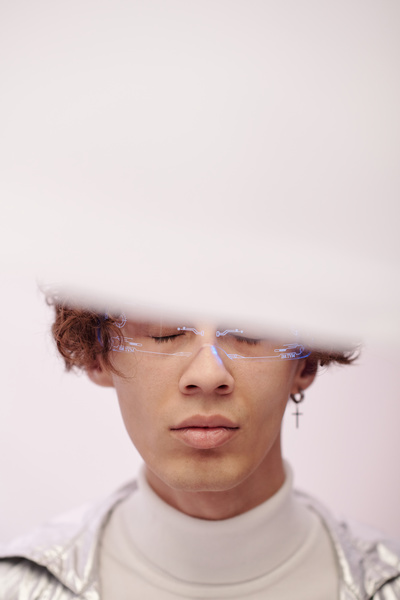 Close-up of a futuristic man with wavy hair wearing glasses with a blue illuminated pattern with closed eyes and upper face hidden