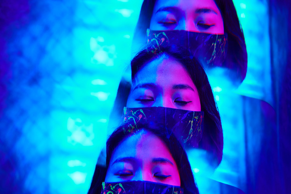 Futuristic image of reflections of a cyberpunk woman's face with closed eyes in a black mask with a colorful print flooded with blue and pink neon light