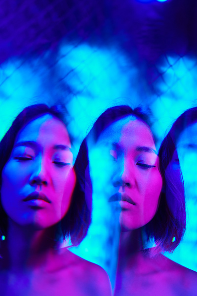 Futuristic image of reflections of a cyberpunk woman's face with closed eyes flooded with blue and pink neon glow with a metallic grid on the background
