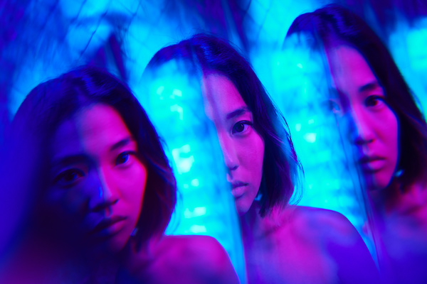 A futuristic image of the reflection of a young female cyberpunk face with dark short hair illuminated by blue and pink neon glow with a metallic grid on the background