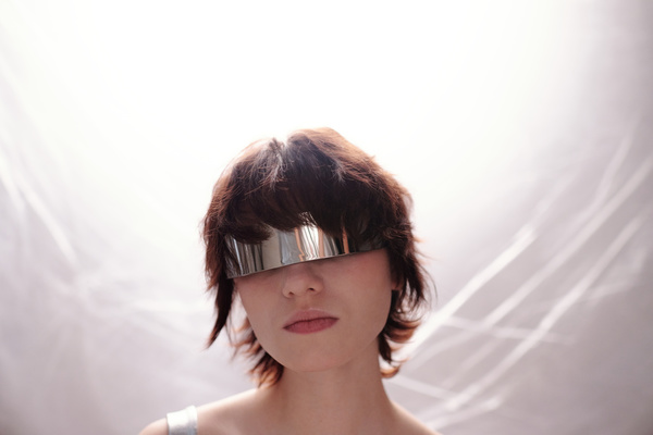 Full-face portrait of a young beautiful woman with short hair in futuristic iron glasses with a bright light on the background