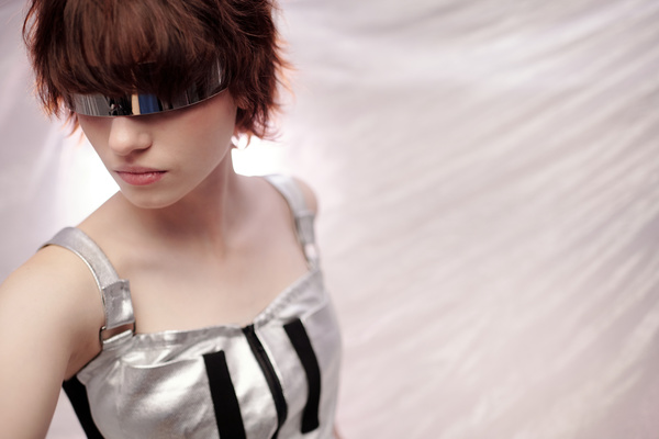 A young woman with wavy brown hair cut in a square in modern attire and metal glasses completely hiding her eyes turned her head to the right