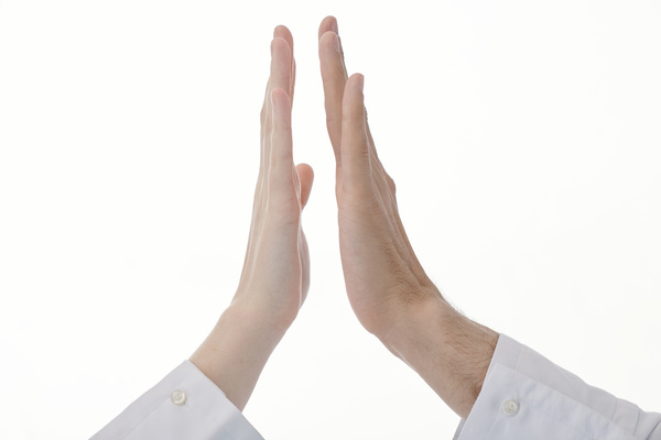 Hands of a man and a woman in white clothes are close to touch against light background