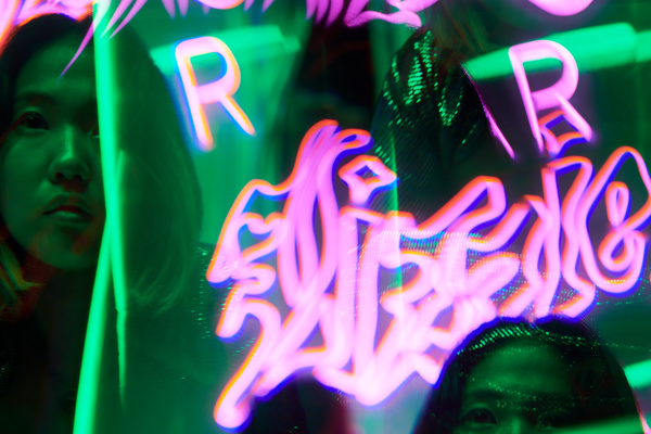 Futuristic image of neon pink graffiti against a background of green rays and lights and the multiple reflections of a young woman with short haircut