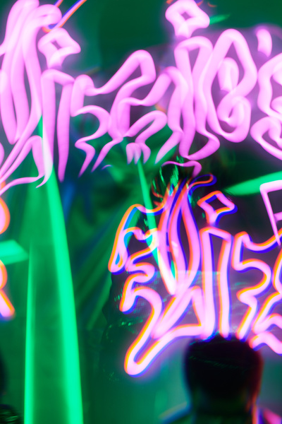 Futuristic image of neon pink graffiti on a background of green beams and lights and the reflection of a man