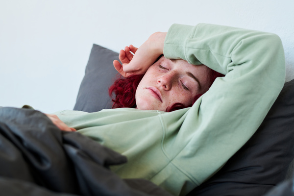 A woman with SARS with brightly colored curls dressed in a light sweatshirt sleeps with her hand covering her forehead