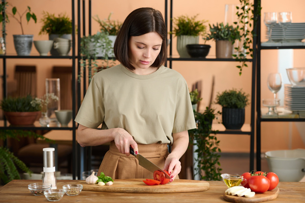 A Woman Is Standing at a Table and Slicing a Tomato