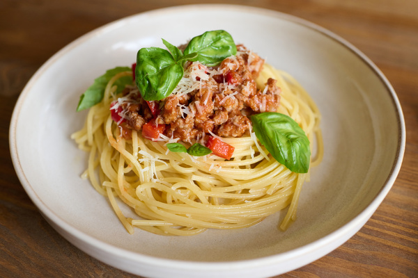 Pasta bolognese garnished with basil leaves in a white plate on a wooden table