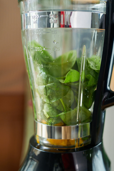Spinach leaves filled with water for making smoothies in a transparent jug of a blender with a black handle