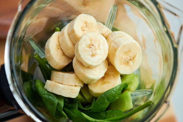 Banana slices and spinach leaves for making smoothie are there in a jug of a blender