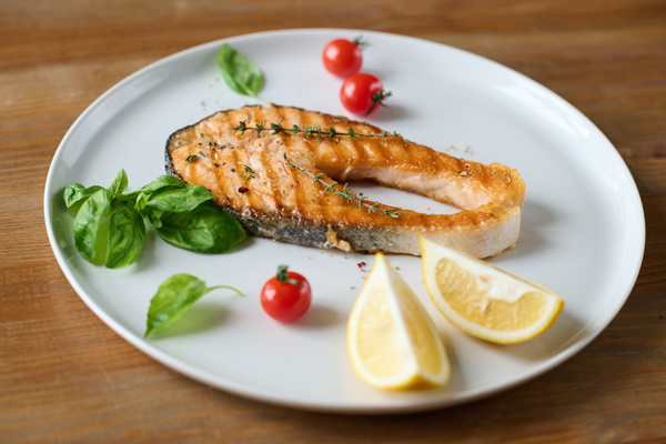 Grilled red fish steak with thyme lies on a white plate with basil cherry tomatoes and lemon slices