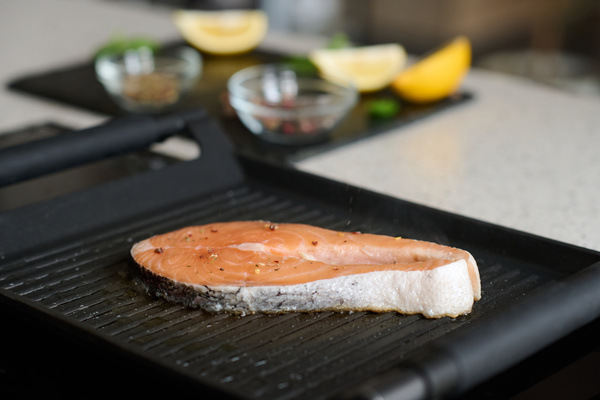 A juicy red fish steak sprinkled with seasonings is fried in a grilling pan of black color