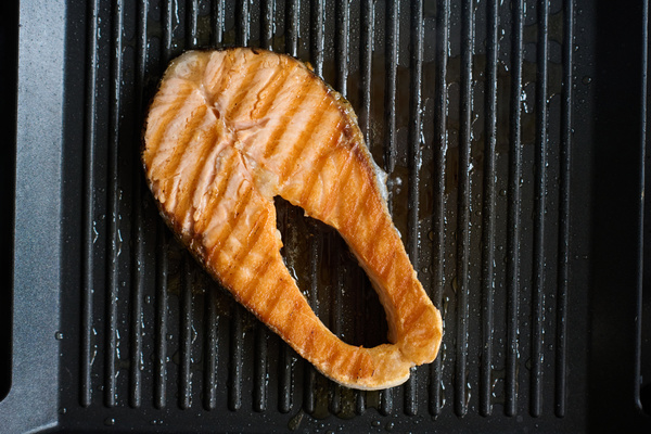 Juicy red fish steak fried in oil lies in a black grill pan