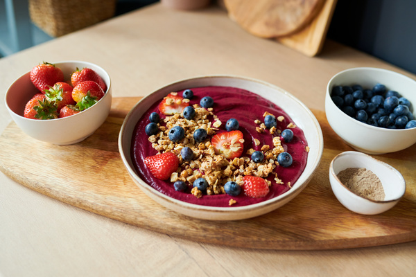 Berry smoothie bowl with granola and berries on a wooden board among plates with blueberries and strawberries and a small bowl with protein powder