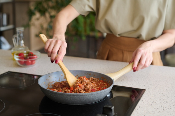 The chef is stirring the bolognese sauce with a chef's spoon  which is cooked in a gray pan