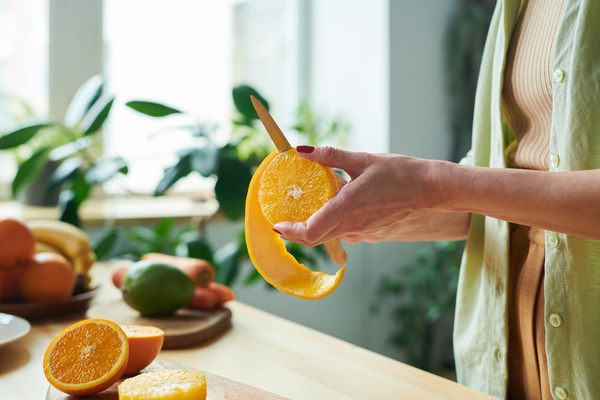 A woman peels half an orange with a small knife over a table on which a orange is cut