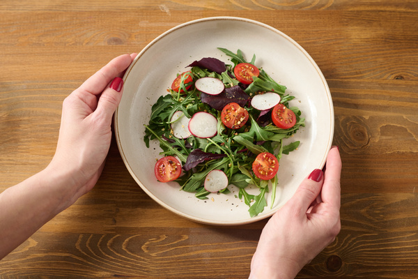 Salad of thinly sliced radishes cherry tomatoes and arugula with basil in a white plate touched by women's hands