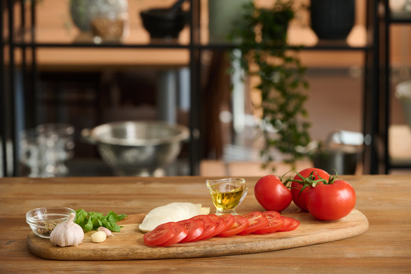 The chopped ingredients of the caprese salad lie on a cutting board made of wood with herbs seasonings and oil in a gravy boat