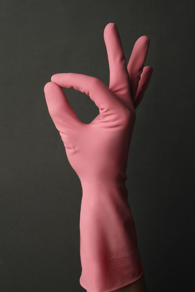 A man shows a OK gesture with his hand in a pink rubber glove on a dark background