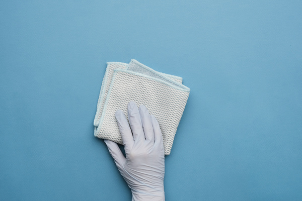 A light cleaning cloth is held in the hand in a blue rubber glove on a blue surface