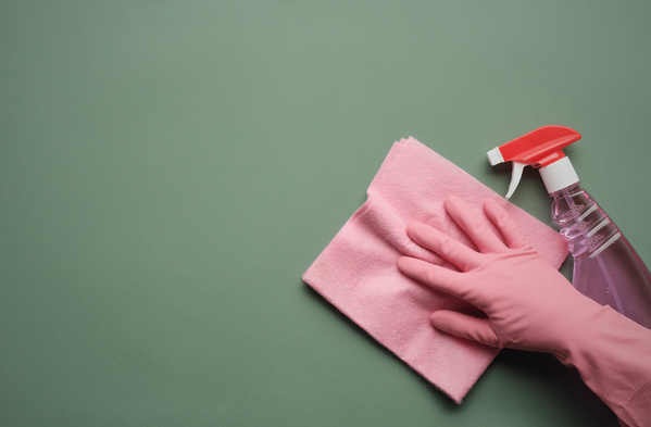 A hand in a pink rubber glove on a pink viscose household napkin and a sprayer with household chemicals
