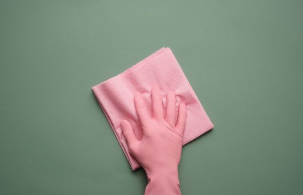A hand in a pink rubber glove on a pink viscose household napkin that is on a green surface