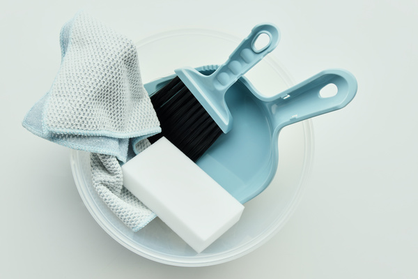 A plastic container with a melamine sponge and a microfiber cloth floor cleaning set of a blue dustpan and a brush with black bristles on a white surface