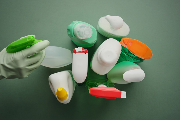 The diffuser surrounded by bottles of detergents is taken in the hand in a green rubber glove