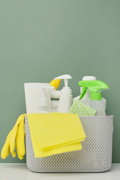 Detergents yellow rubber gloves and a green sponge are stacked in a light-colored plastic basket