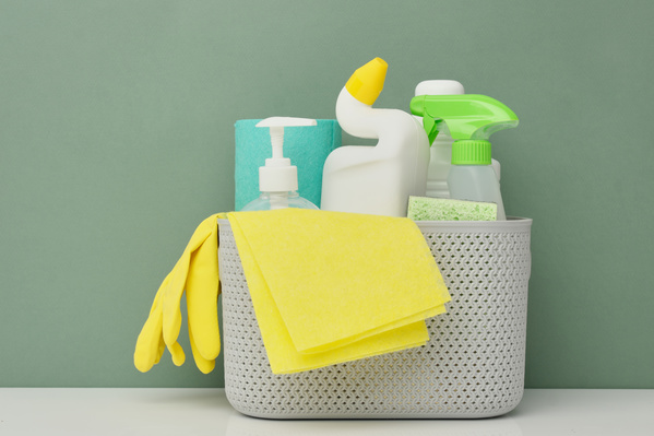 Detergents yellow rubber gloves and a wiper cloth are in a light-colored plastic basket