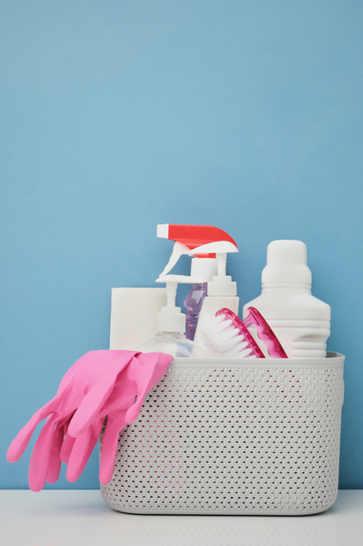 Household chemicals with pink rubber gloves and an iron scrubbing brush in a white plastic basket