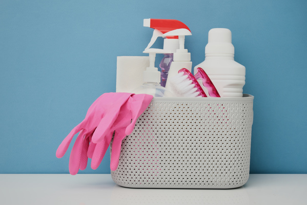 Cleaning products with pink rubber gloves and a scrubbing iron brush in a white plastic basket