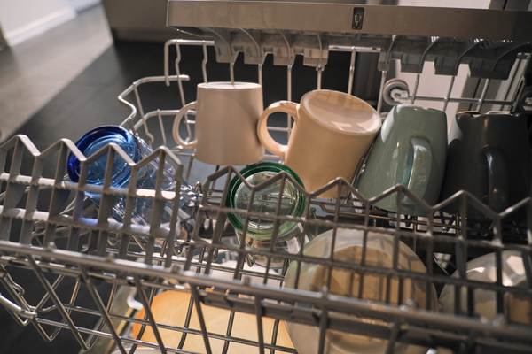 Mugs and glasses of different colors on the grates in the dishwasher in the bright kitchen