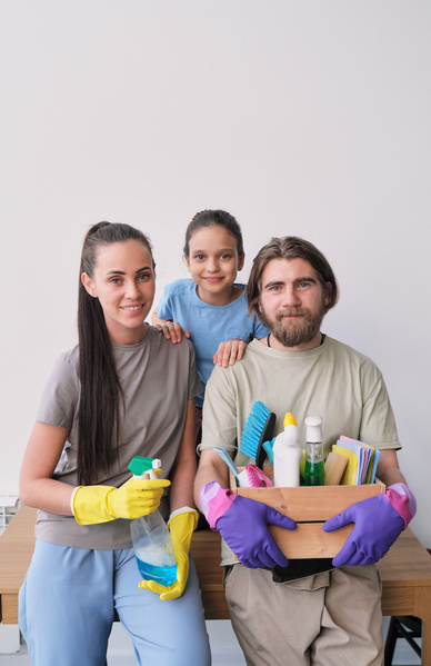 Photo of a young family with one child in rubber gloves with a cleaning kit and a sprayer filled with household chemicals in their hands